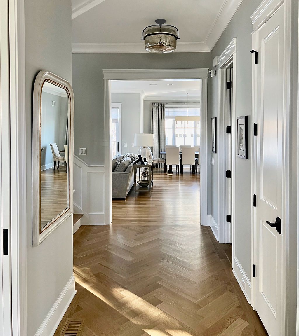 Hallway with herringbone wood floor, light blue walls, and a mirror. Leads to living and dining rooms.