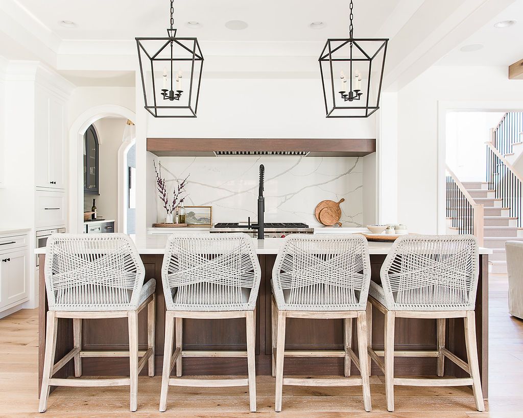 Kitchen island with four woven-backed bar stools, two hanging geometric lights, and a backsplash.
