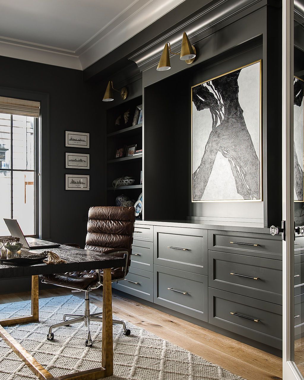 Dark, elegant home office with built-in cabinetry, desk, leather chair, and abstract art.