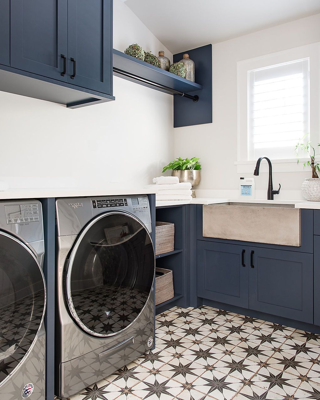 Laundry room with navy cabinets, stainless steel machines, patterned floor, and white countertop.