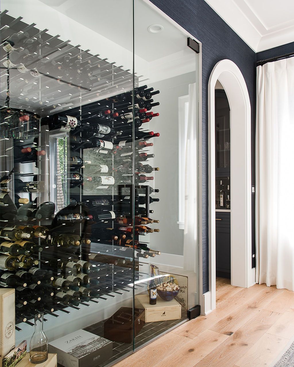 Wine cellar with glass door, dark bottles, and reflective mirrored wall.