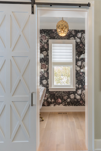 White barn door partially open revealing a room with floral wallpaper and a window.
