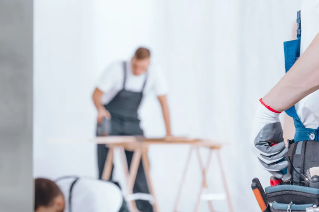 Workers assembling furniture in a bright room, with tools in the foreground and a table in the background