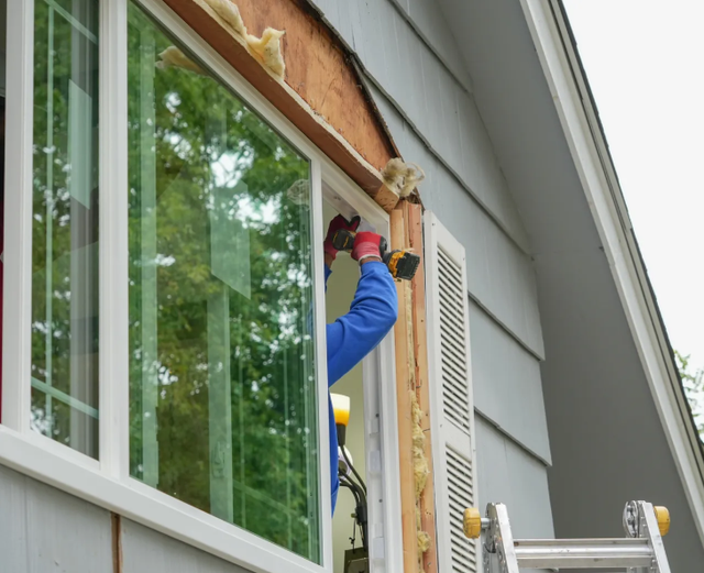 Worker on ladder installing trim beside a house window and vent