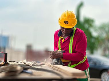 Construction worker in yellow hard hat and pink vest working outdoors at a site