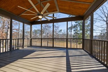 Covered wooden deck with ceiling fan and railings, overlooking a wooded yard