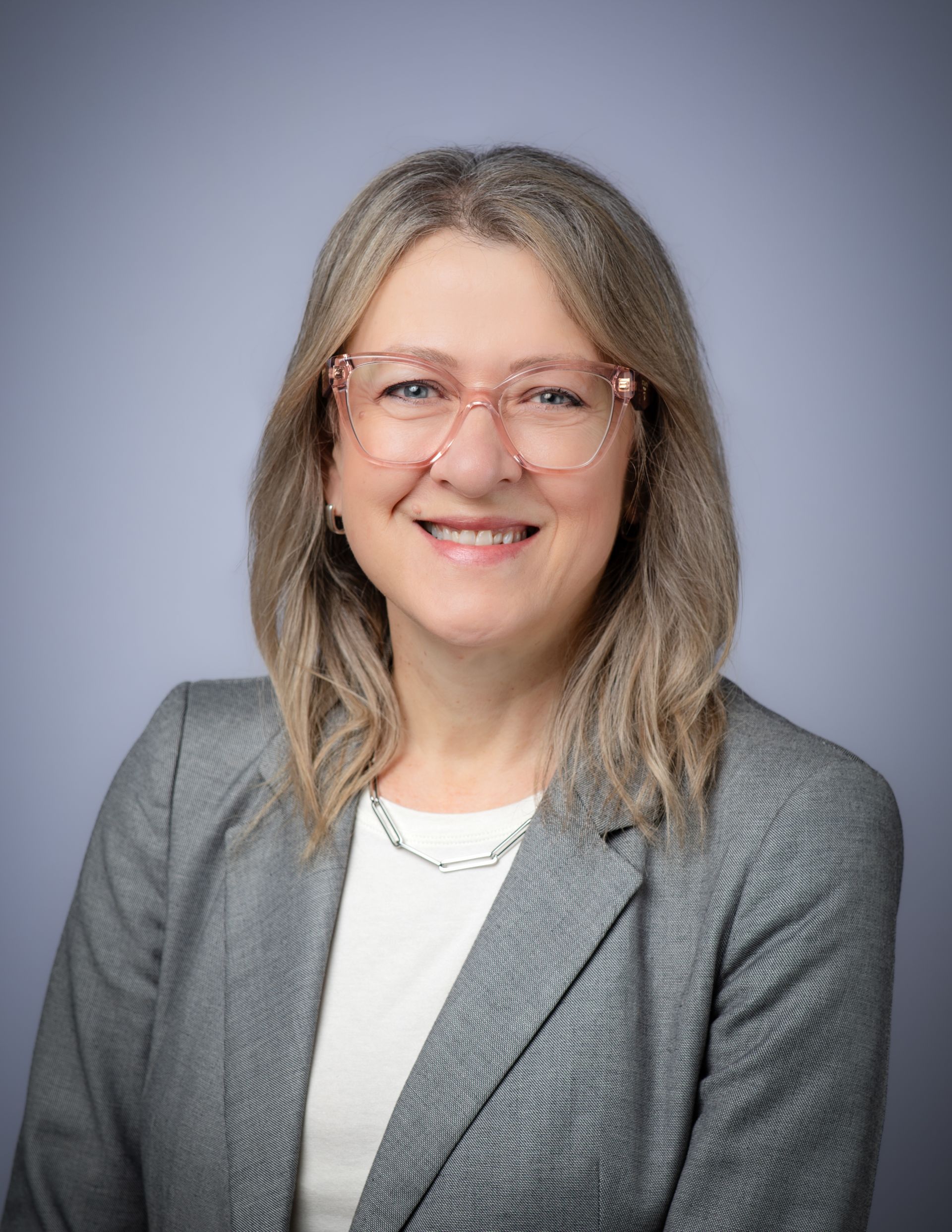 A woman wearing glasses and a white jacket is standing in front of a window | Barbara Hicks