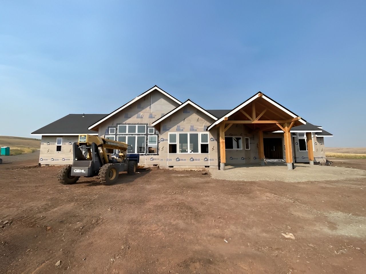 A house under construction with a bulldozer parked in front of it.