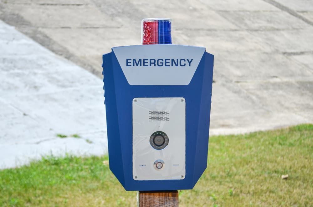 A Blue Emergency Box is Sitting on a Wooden Post in the Grass — BNCC Security Services in Port Macquarie, NSW