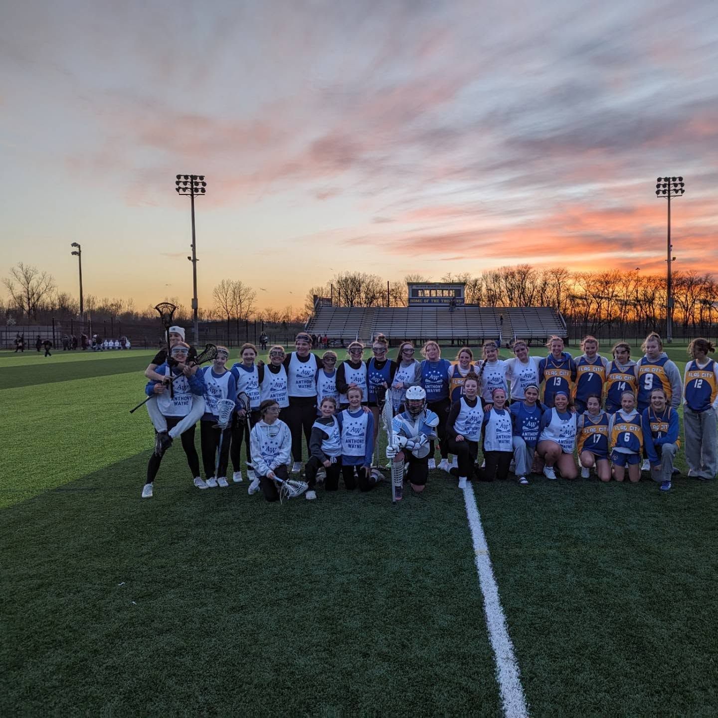 Youth sports team posing on a field at sunset beneath a pink-orange sky.