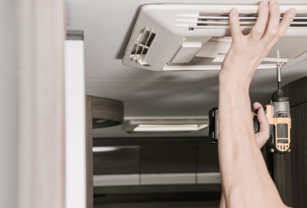 Person Using a Drill to Install or Repair an Air Conditioning Unit Inside a Camper — Lakeside Gas Fridges In Maitland, NSW