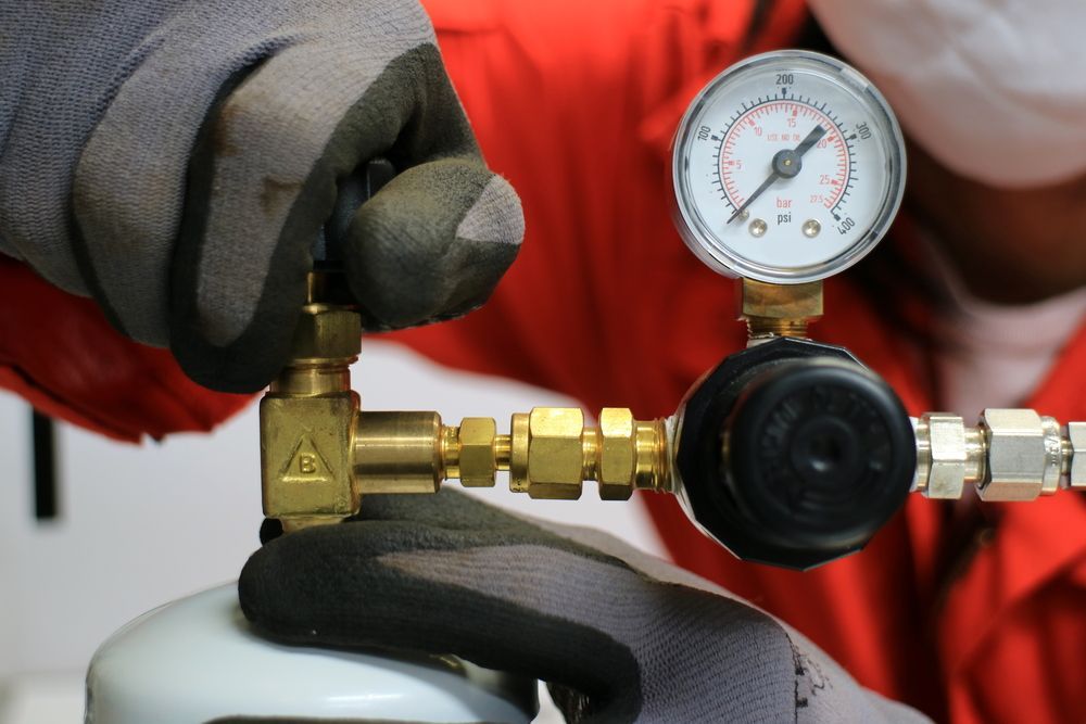 Person in Red Overalls and Gloves Adjusting a Regulator — Lakeside Gas Fridges In Maitland, NSW