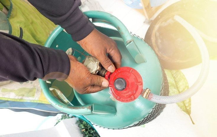 Hands Attaching a Red Regulator to A Green Propane Tank — Lakeside Gas Fridges In Argenton, NSW