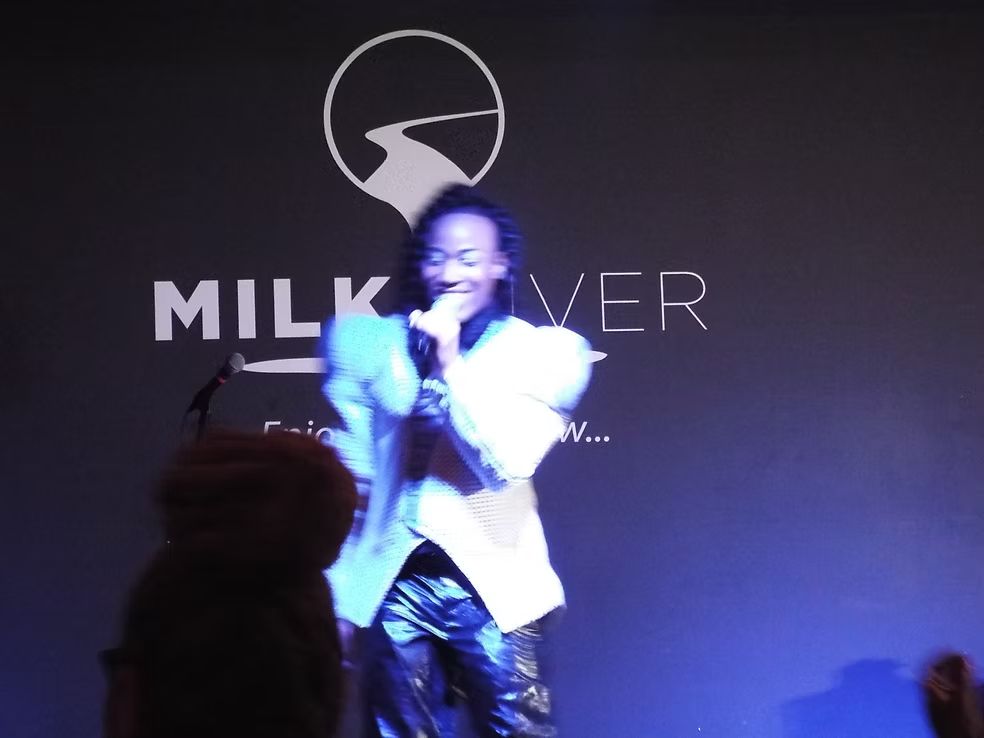 Singer performing on stage in front of a MILKIVER backdrop, lit in blue light