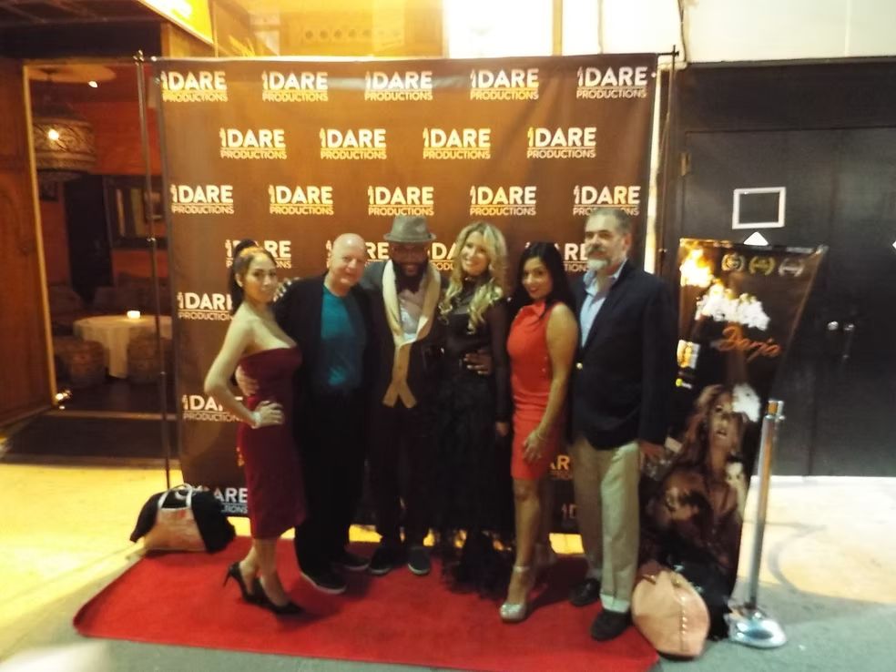 Group posing on a red carpet in front of an IDARE backdrop, with a dog in a pink outfit at the right.
