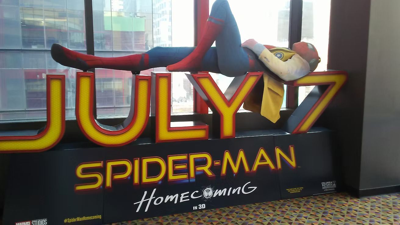 Movie display for Spider-Man: Homecoming with a large red-and-yellow “JULY 7” sign and Spider-Man figure lounging above it