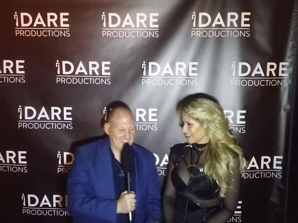 Two people speaking at a DARE Productions event before a branded backdrop