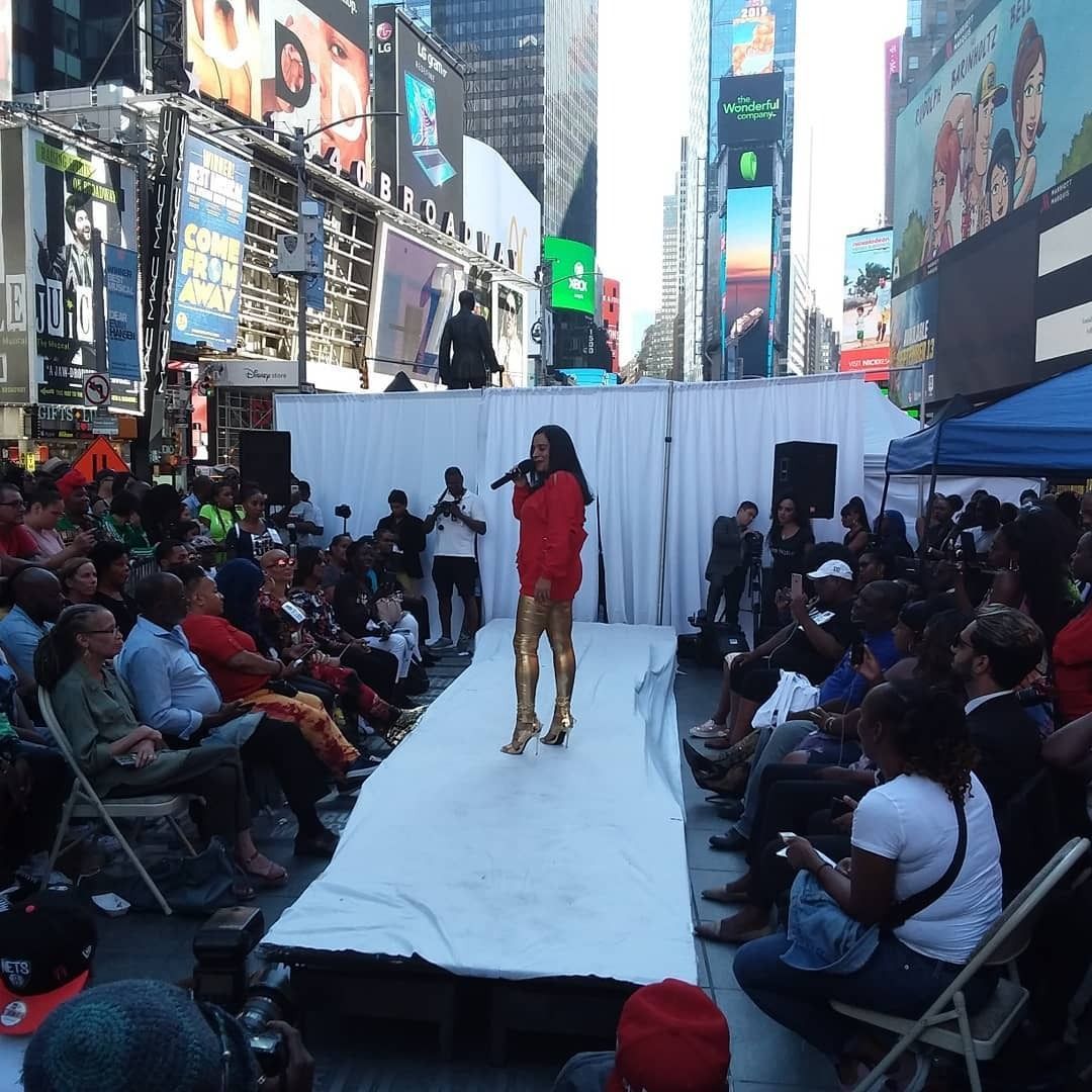 Street performer in red on a white runway in a crowded Times Square plaza, surrounded by seated spectators