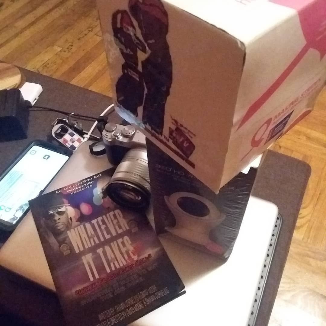 Magazines and a camera on a table beside stacked boxes in a living room.