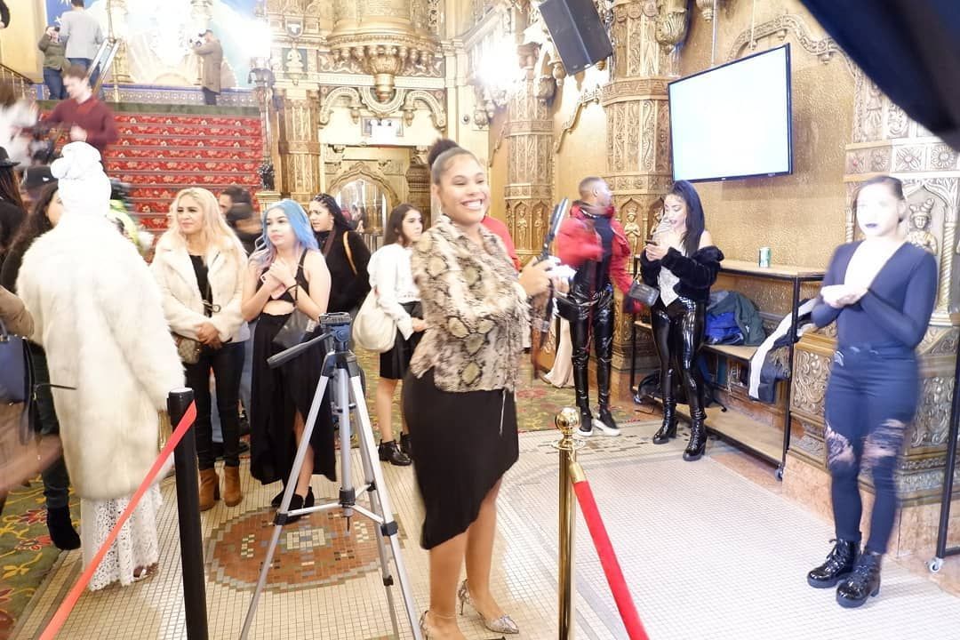 Visitors queue inside a decorated historic room with velvet ropes, cameras, and ornate gold walls.