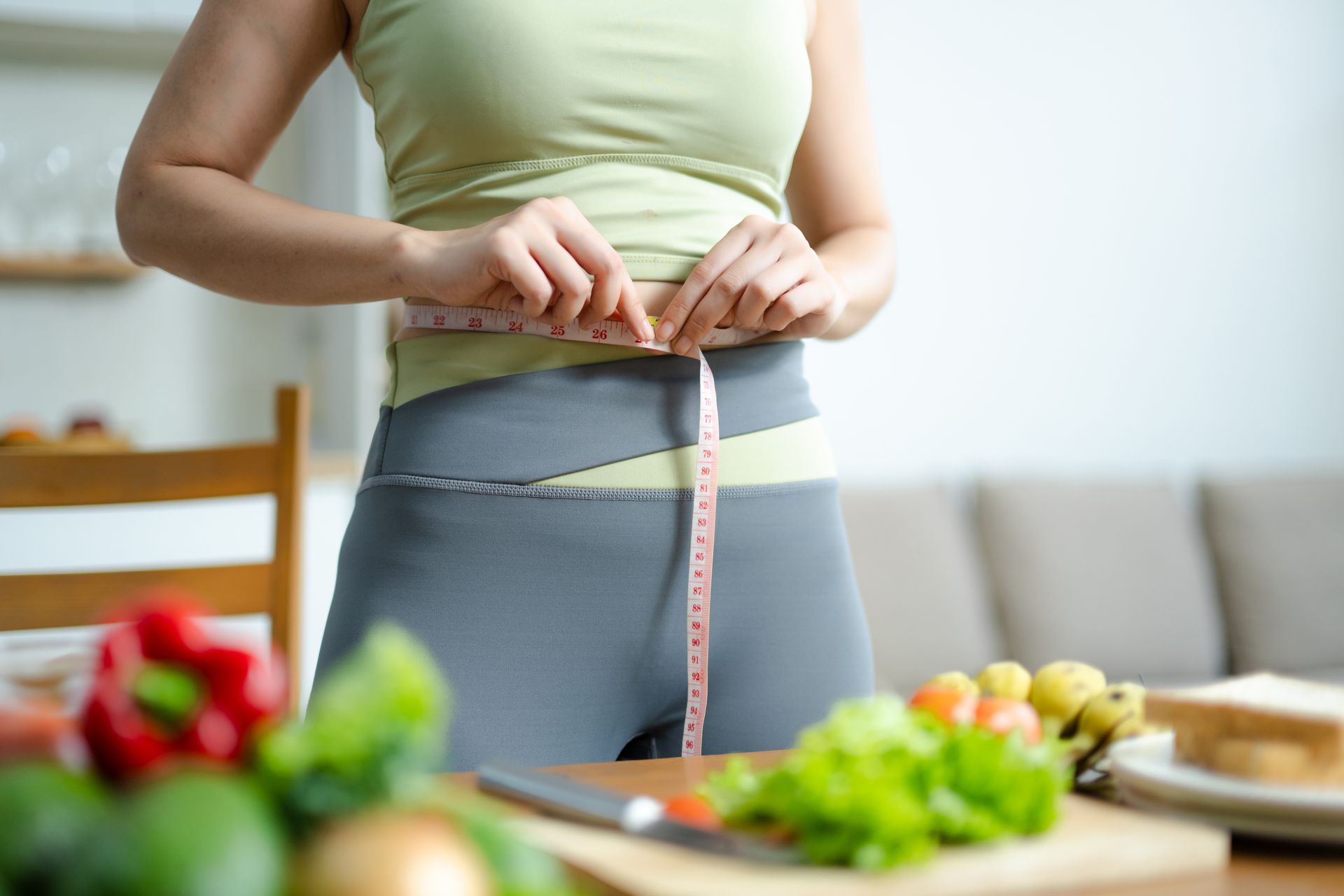 Woman measuring her waist beside fresh vegetables, weight loss programs in Maryville, TN.