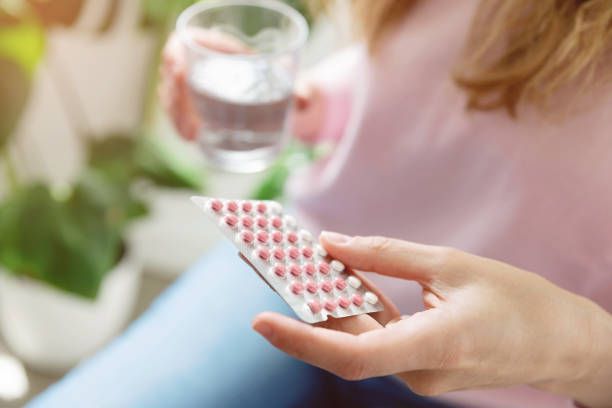 Woman holding a blister pack of pills, about to take one with a glass of water.