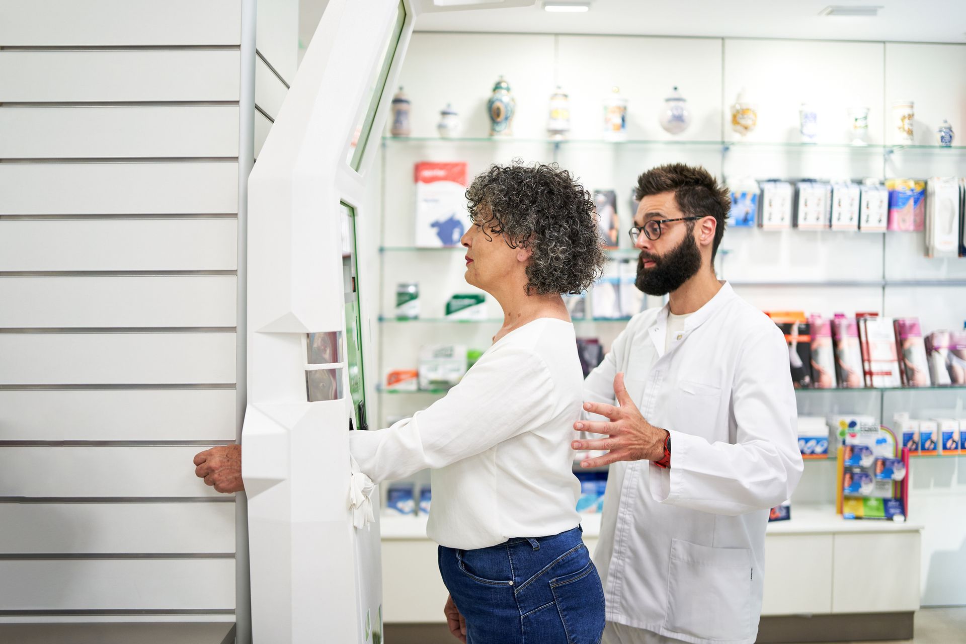 Woman using health machine for medical weight loss services with pharmacist assisting in pharmacy. Woman using health machine for medical weight loss services with pharmacist assisting in pharmacy.