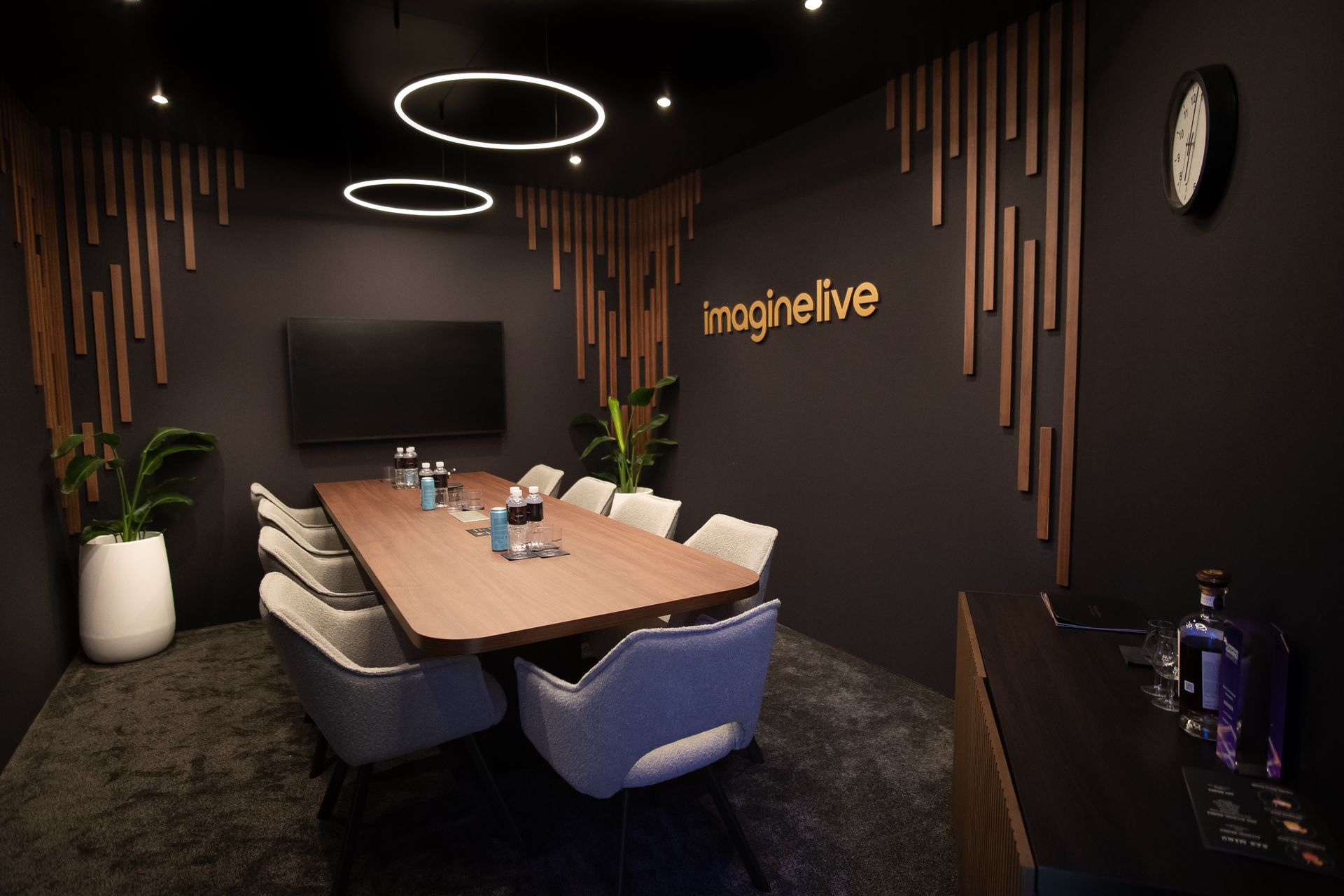 Modern conference room with a long table, blue chairs, wall TV, and circular ceiling lights