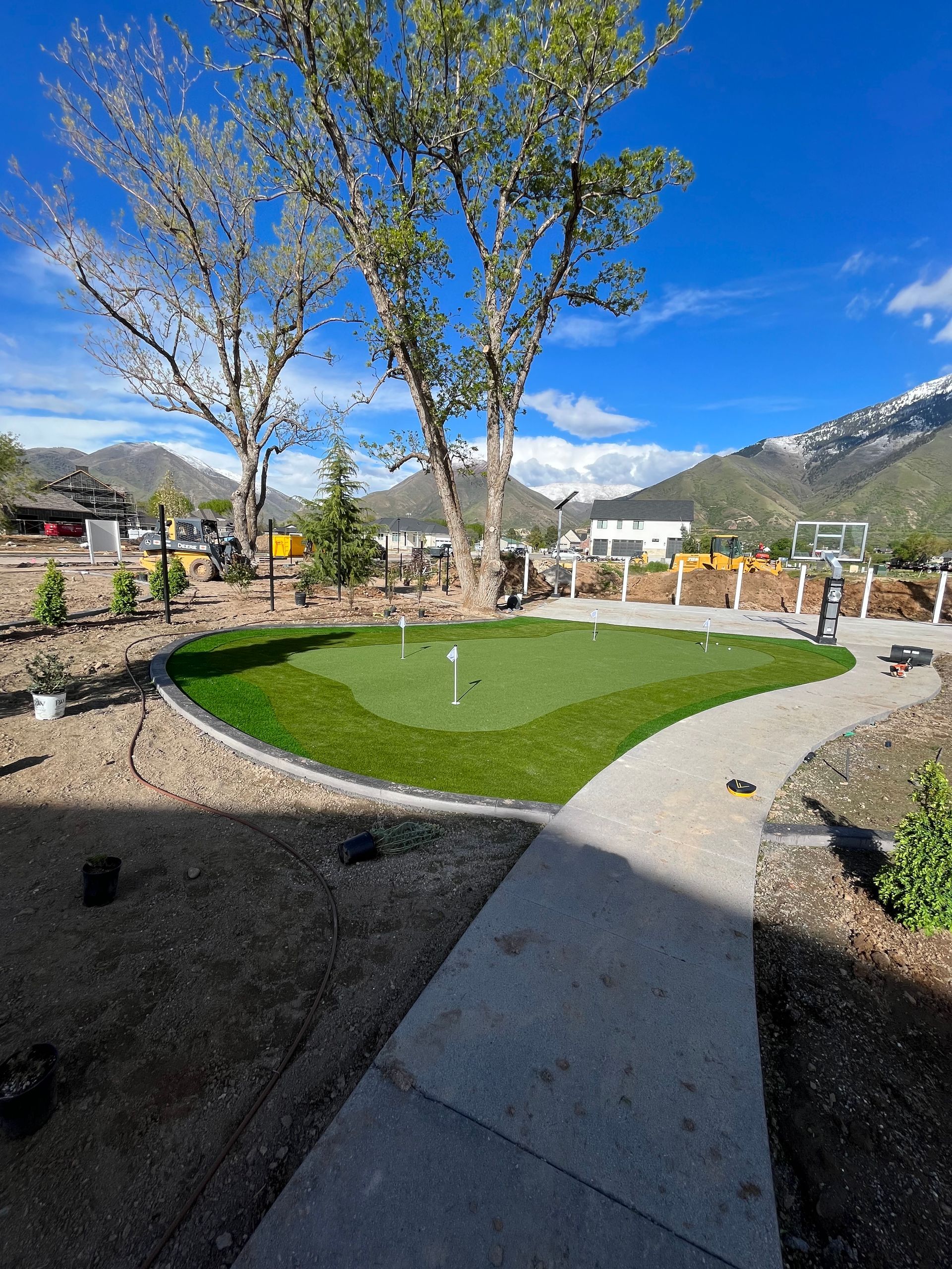 A putting green with flags, surrounded by tan gravel and a walking path, under a blue sky.