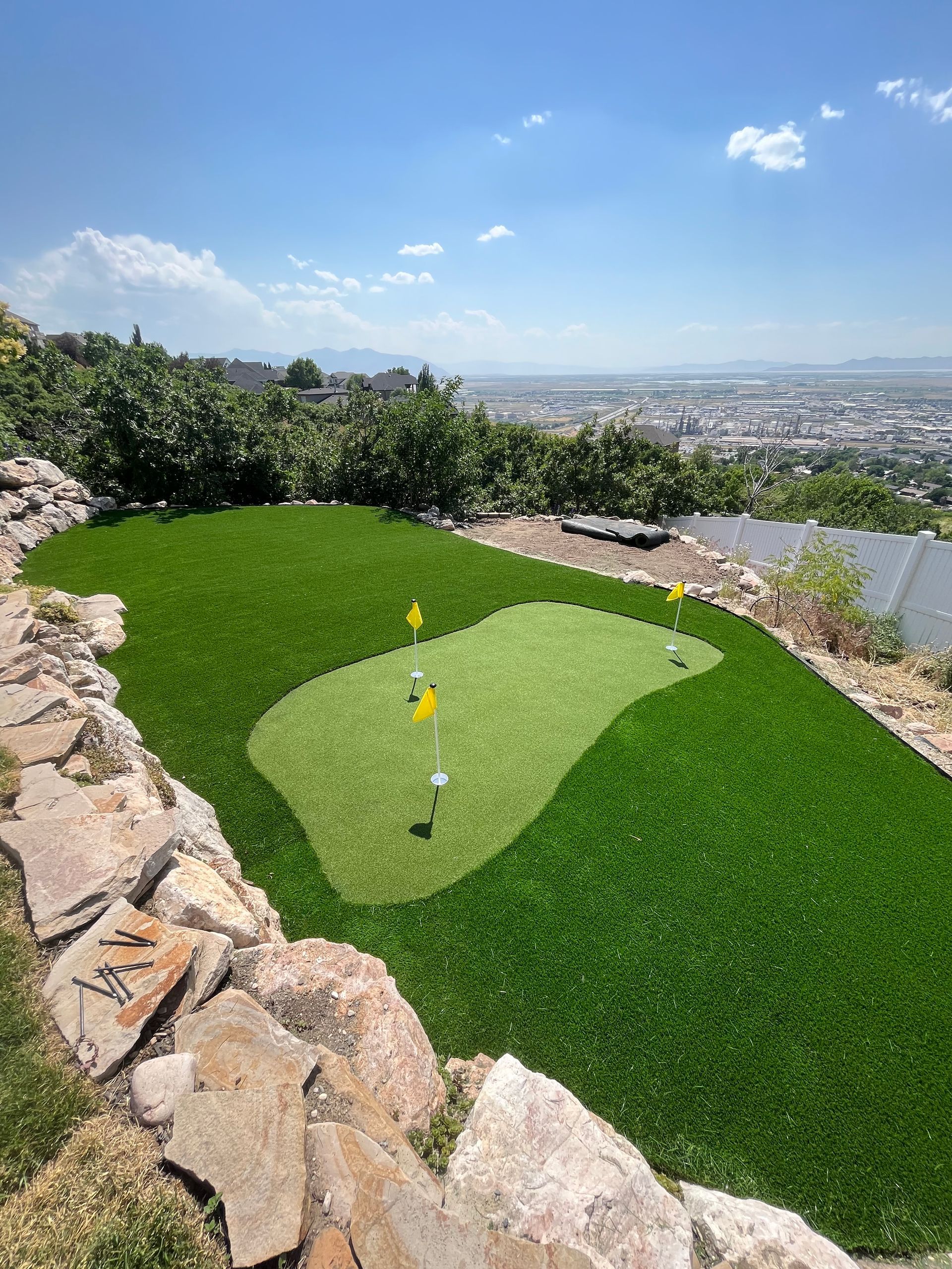 Green golf putting green with flags, golf balls, and cityscape in the background.