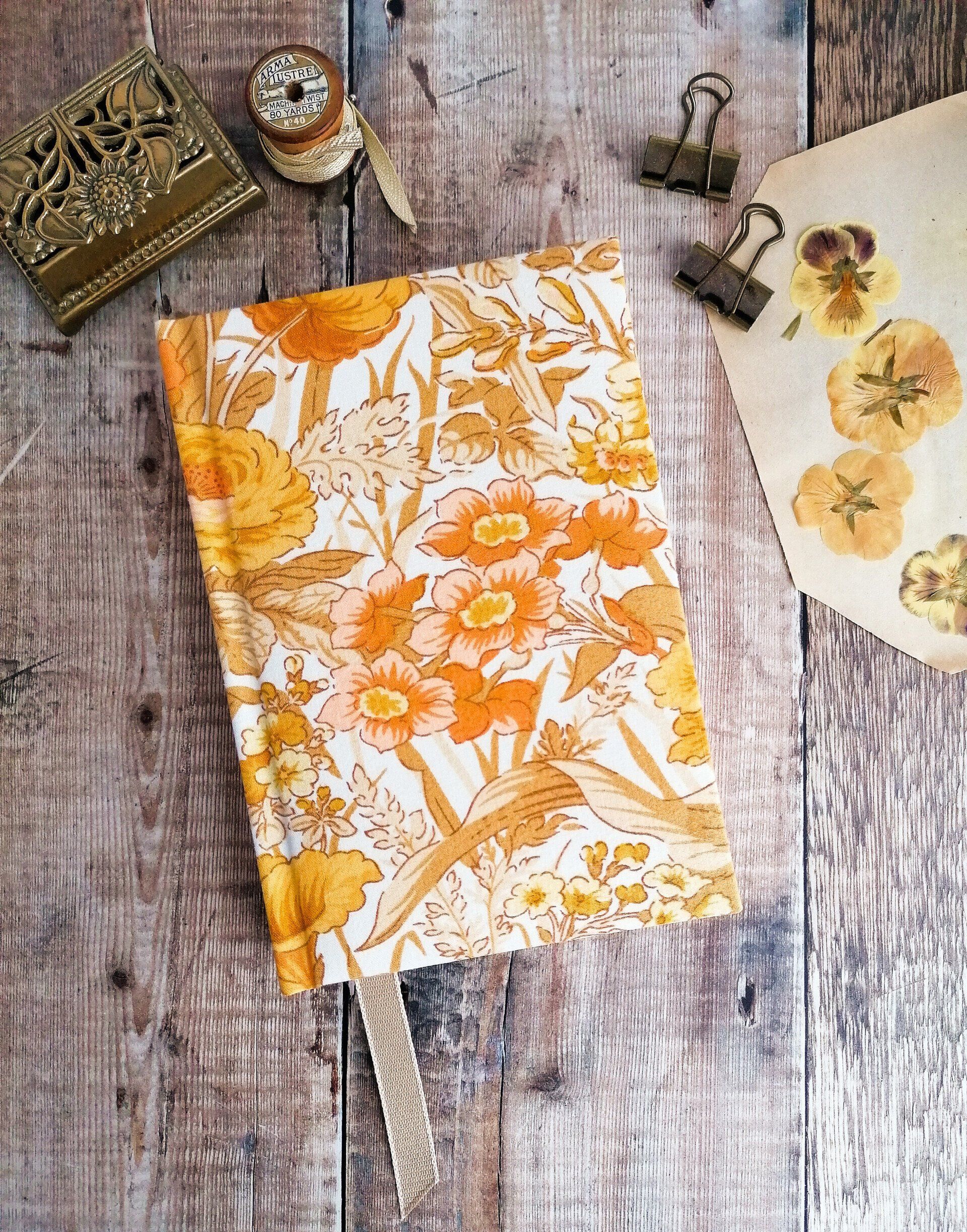 An image of a 5 year diary A5 size made with upcycled vintage fabric book covers and decorative page marker in light brown. The floral pattern on the book covers is orange peach and tan brown colours on a white background. An Anniversary gift and diary planner. The 5 year diary is laid flat on on rustic wood back ground.