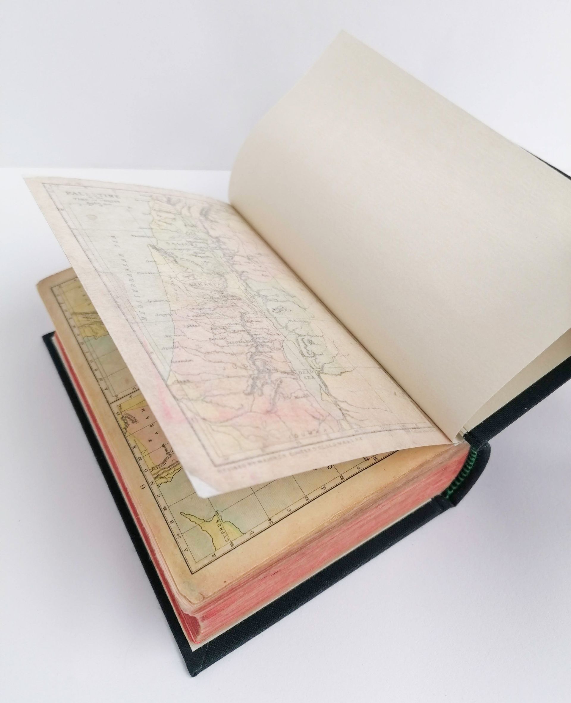 The image shows the back of the repaired book. The back cover is open and the pages are neat and repaired. A map is the back page of the book and the rips on the map have now been repaired. The map now looks smooth and is attached to the book. The book sits on a white background.
