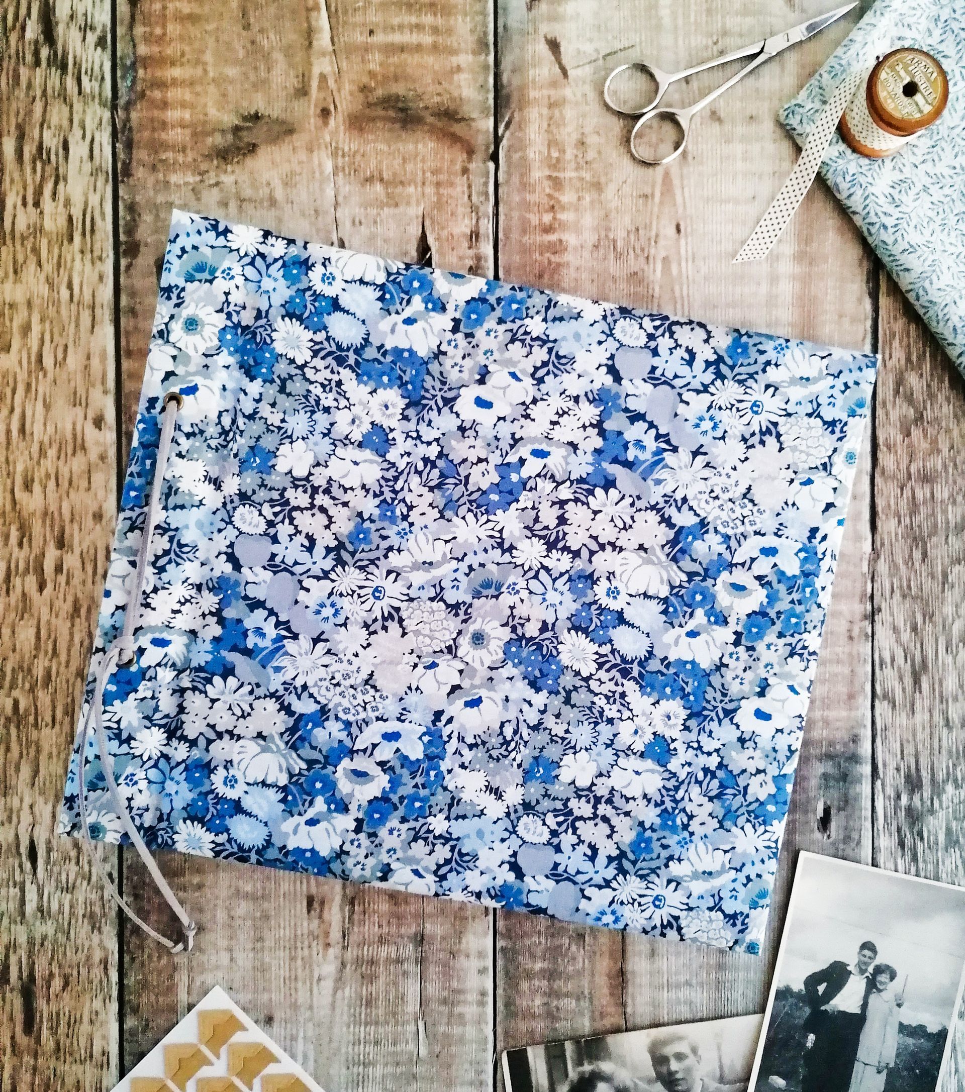 An image of a large album made with upcycled vintage fabric book covers. The floral pattern on the album covers is light blue dark blue lilac and white. The album is landscape and laid flat on a rustic wood back ground. The fabric is by Liberty of London.