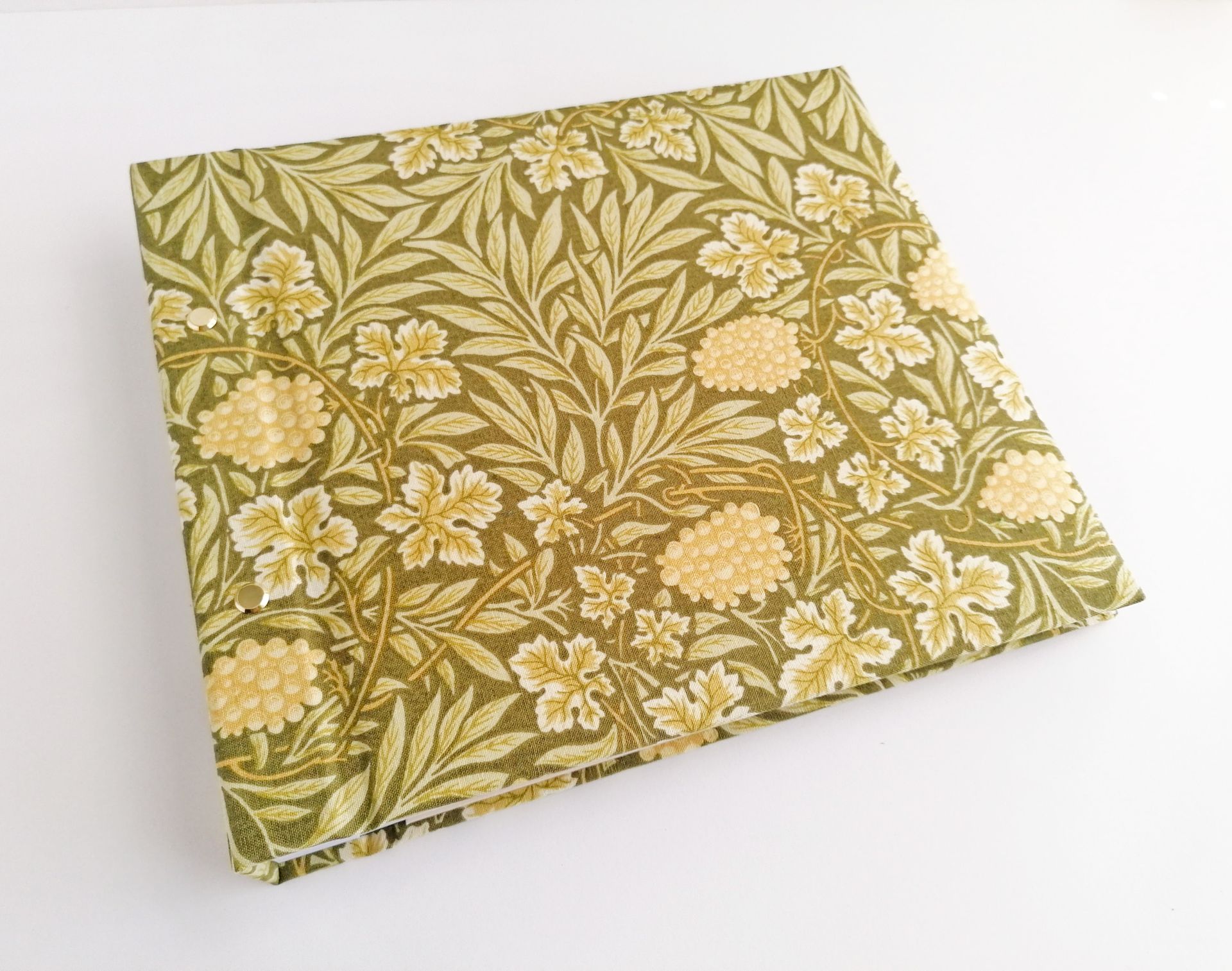 The image shows a large hand made album for photos. The album is covered in a cloth which is green and yellow florals in a vintage style pattern.
