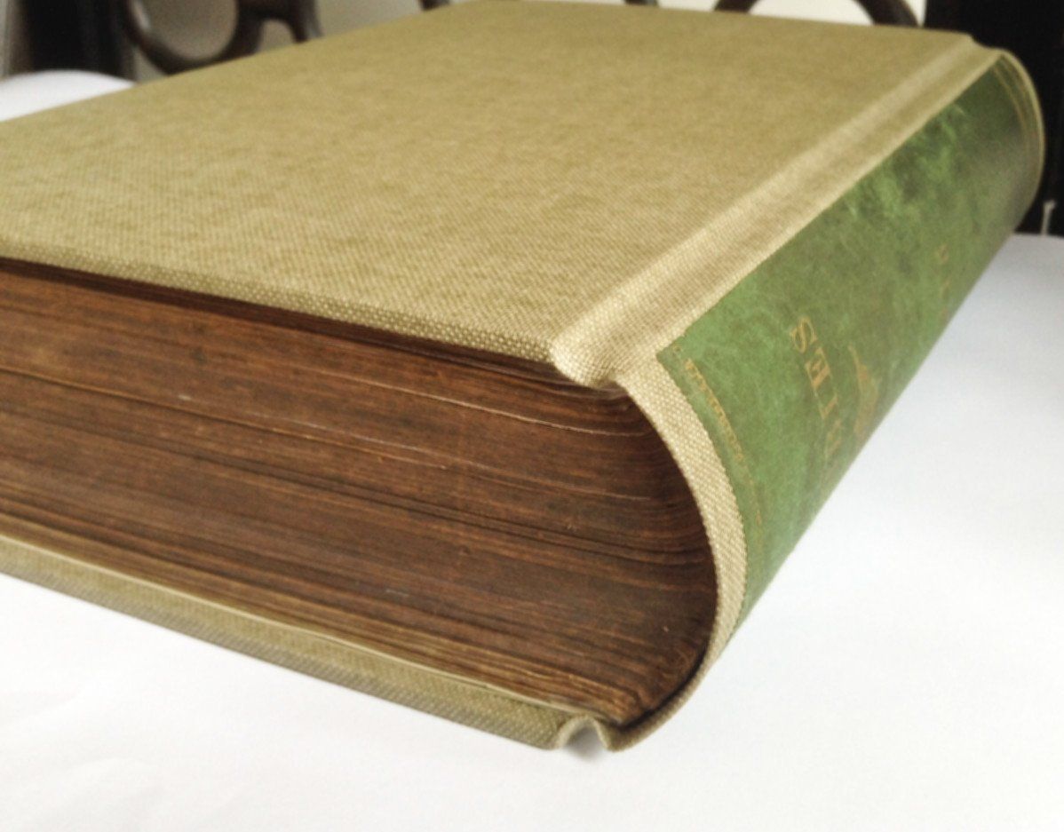 The image shows a repaired green vintage book of Hobbies. The image shows the detail from the top of the book where the pages are neatly in place and the spine is curved and rounded as it traditionally would have been. The original green cover from the spine area has been attached to the new book so that this now has the lettering on the spine.