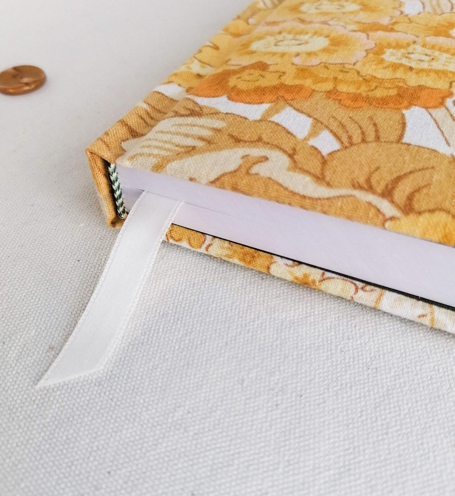 A close up image of a vintage retro yellow and orange floral fabric A6 pocket diary. The diary has padded covers and a white ribbon page marker. It is laid on a plain white background.