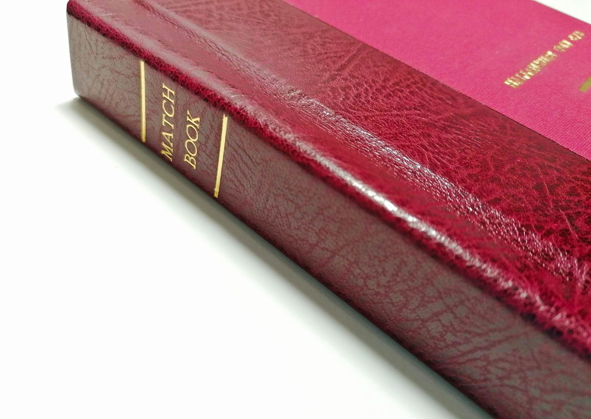 The image shows a red leather hardback flat spine with gold lettering in capital letters which reads 'Match Book'. The book is laid on a white background.