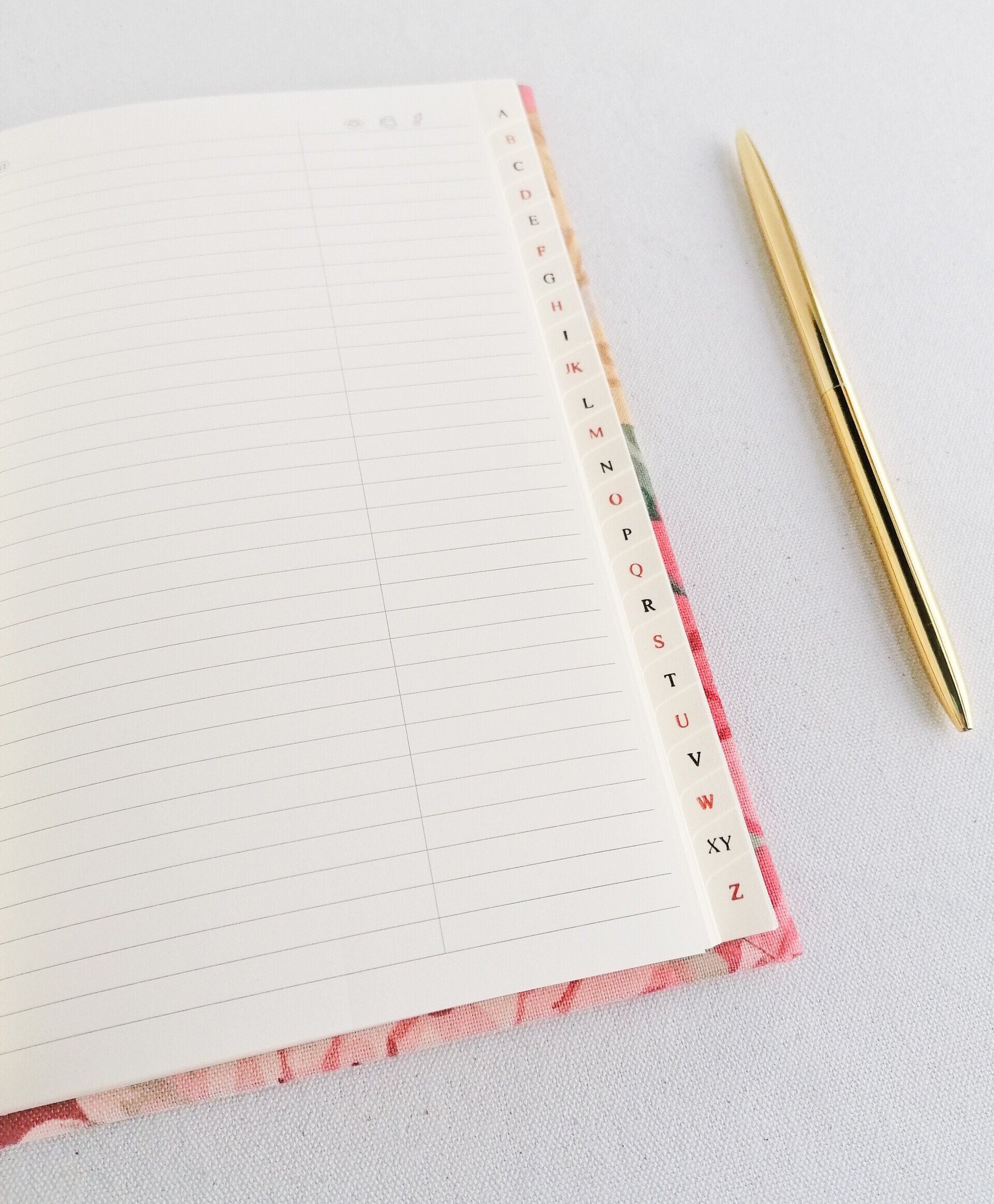 A close up image of a vintage Sanderson fabric A5 address book. There is detail shown of the white address book pages. It is laid on a plain white background. There is a gold pen laid next to the book.