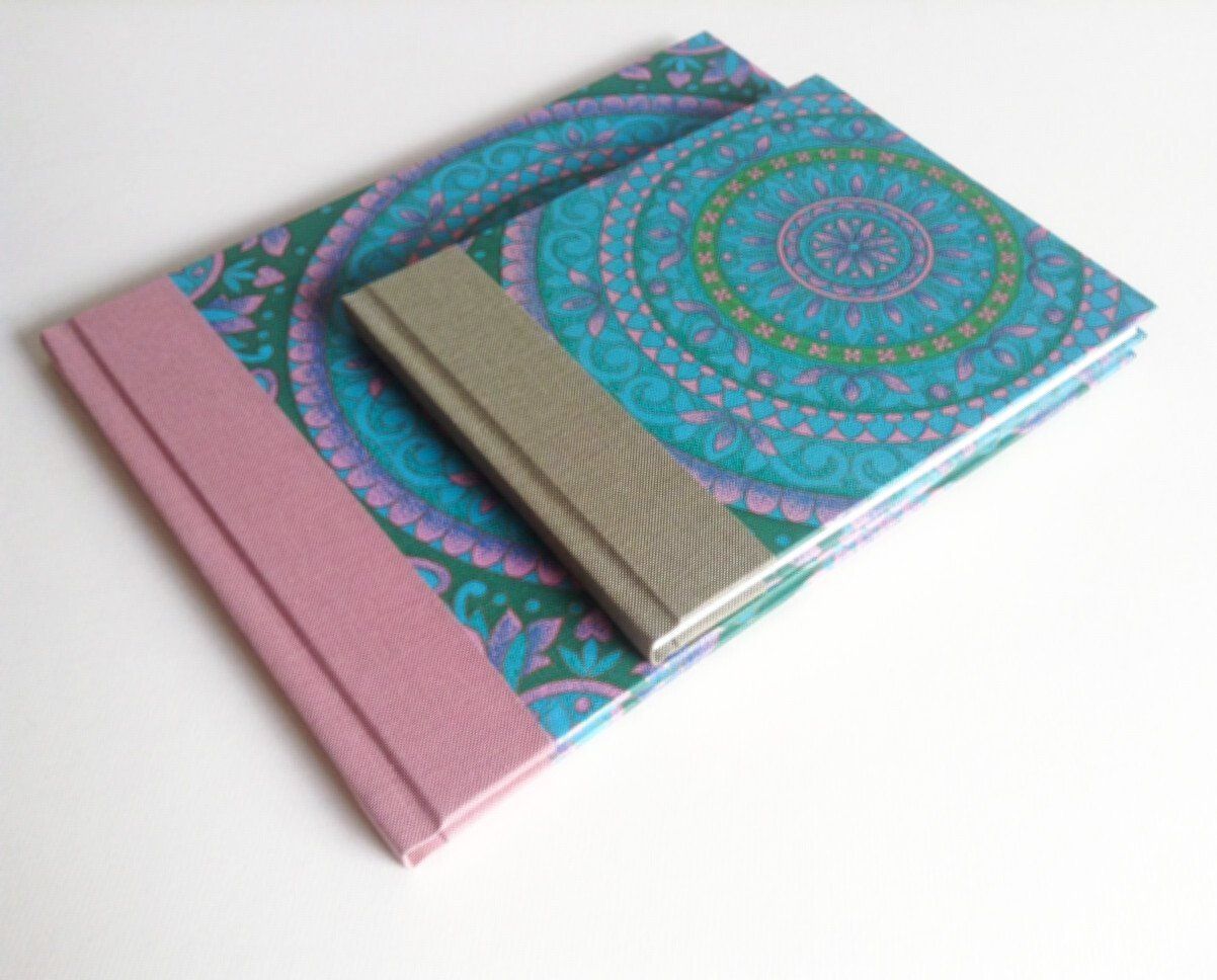 The image shows 2 books on top of one another. One book is large and the one on top is smaller. Both are landscape and covered in a vintage psychedelic patterned wallpaper which is from the 1960's. The colours of the wallpaper are green pink purple and blue in circle patterns.
