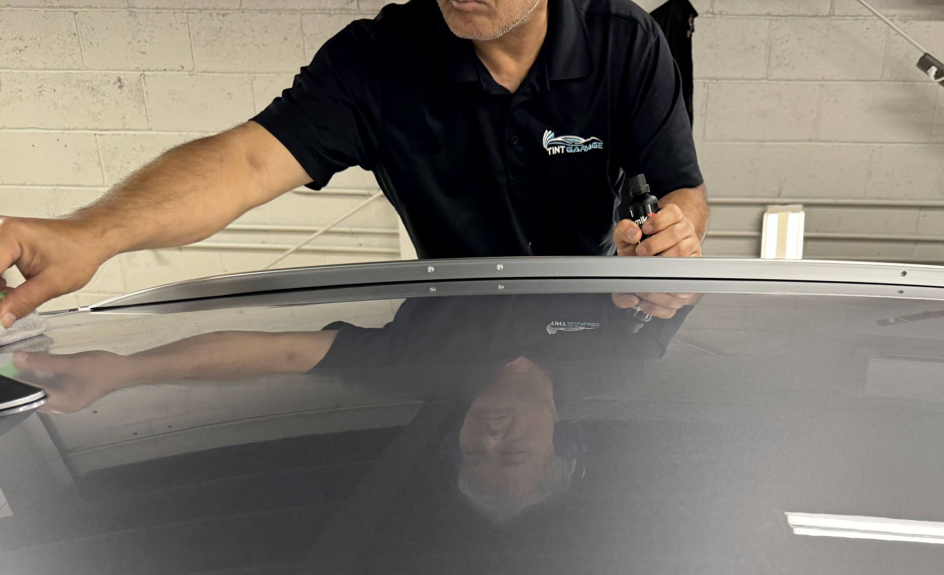 Person in black shirt working on a gray car roof inside a garage