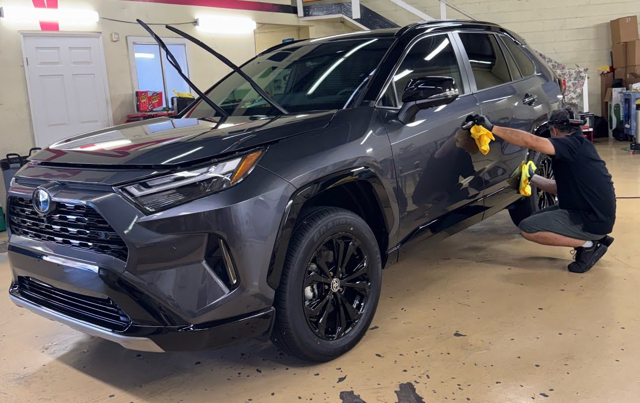 Mechanic polishing the side of a dark gray SUV in an auto shop