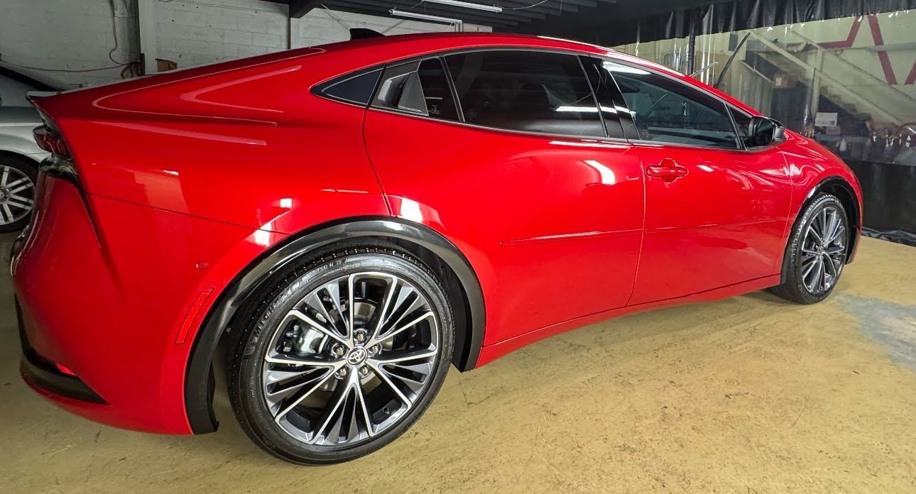Red sports coupe parked indoors, side view with glossy paint and alloy wheels.