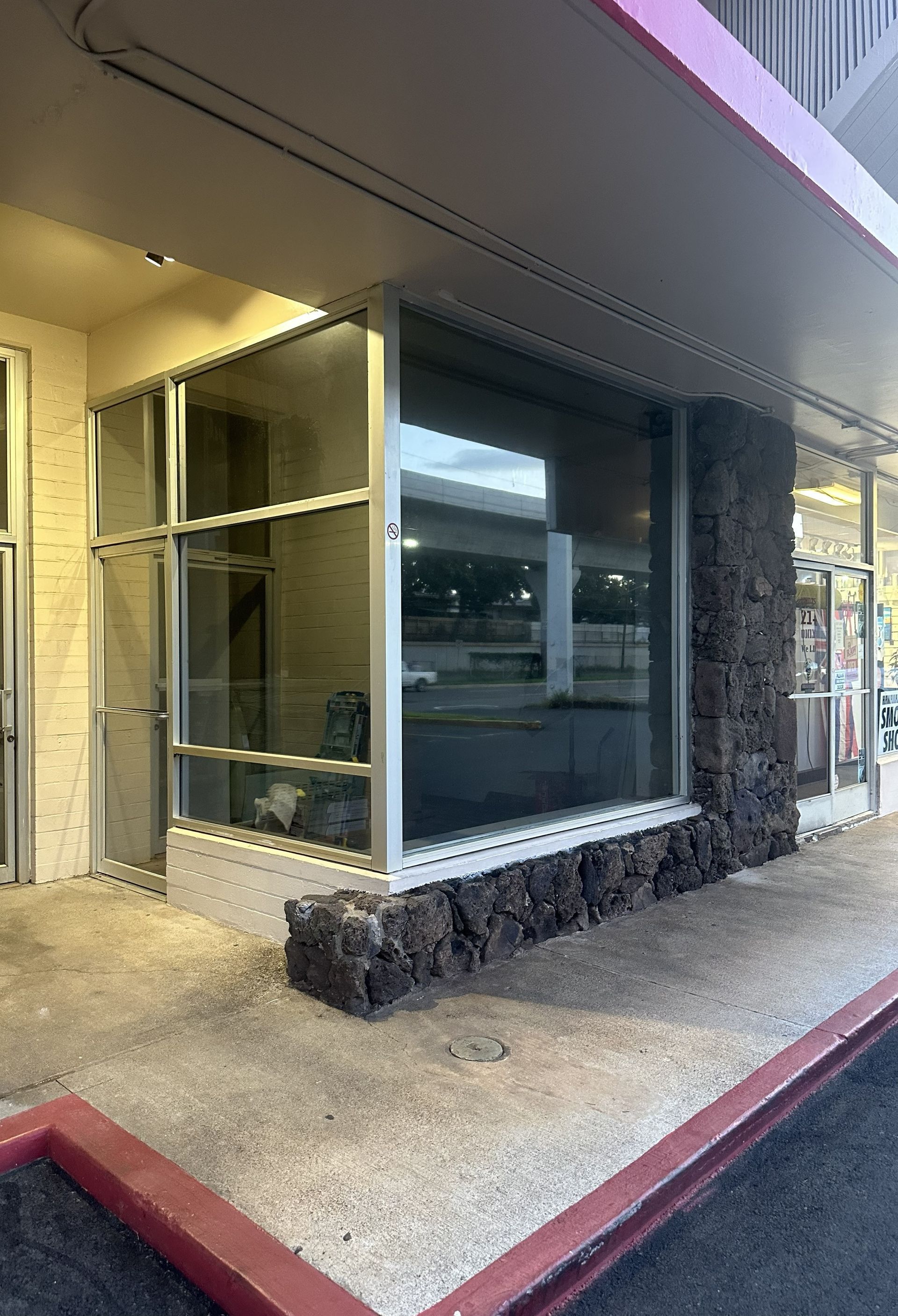 Storefront with large reflective windows and stone trim under an overhang in a covered walkway.