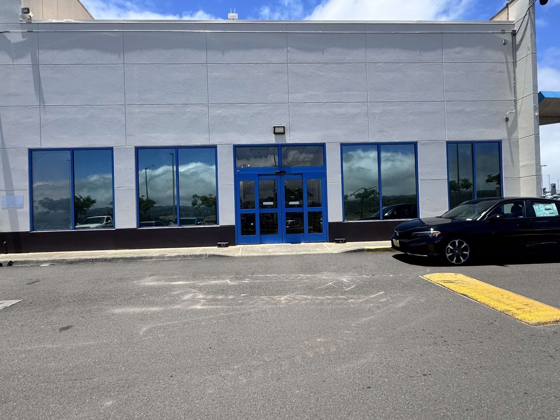 Front view of a gray storefront with blue doors and windows, with a black car parked outside.