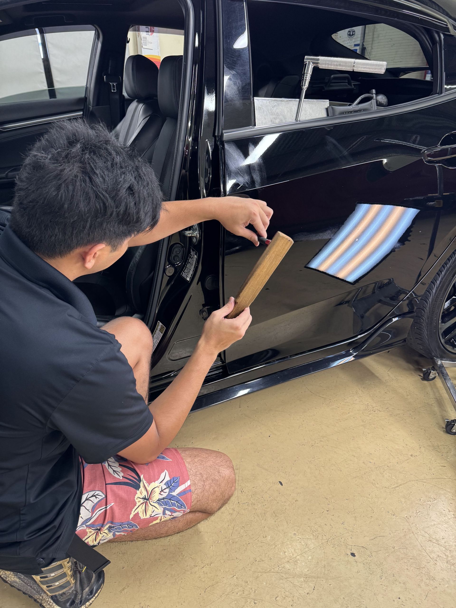 Person kneeling beside a black car, measuring the open door area with a wooden ruler.