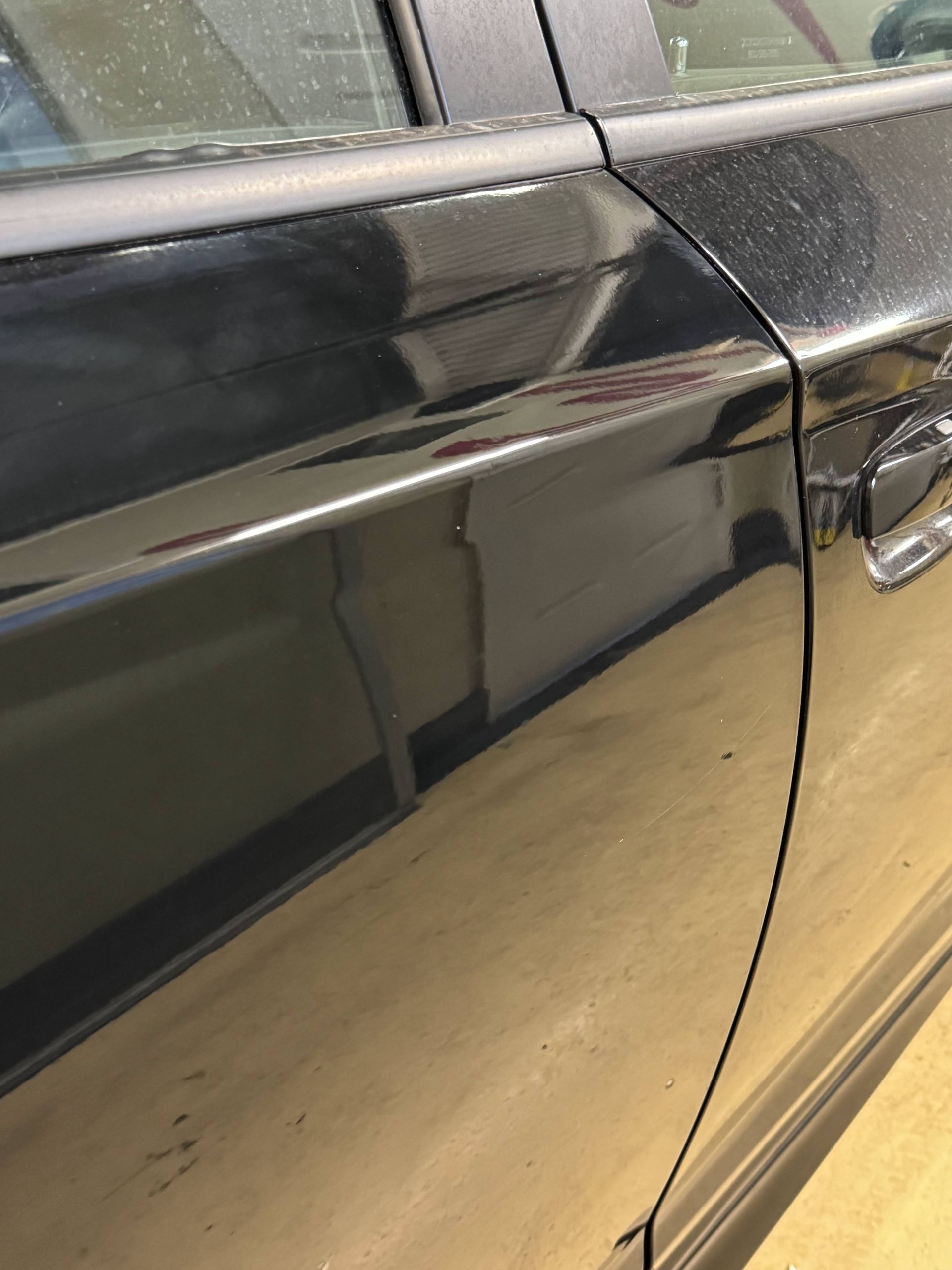 Close-up of a black car door with a visible scratch and reflection on the glossy paint.