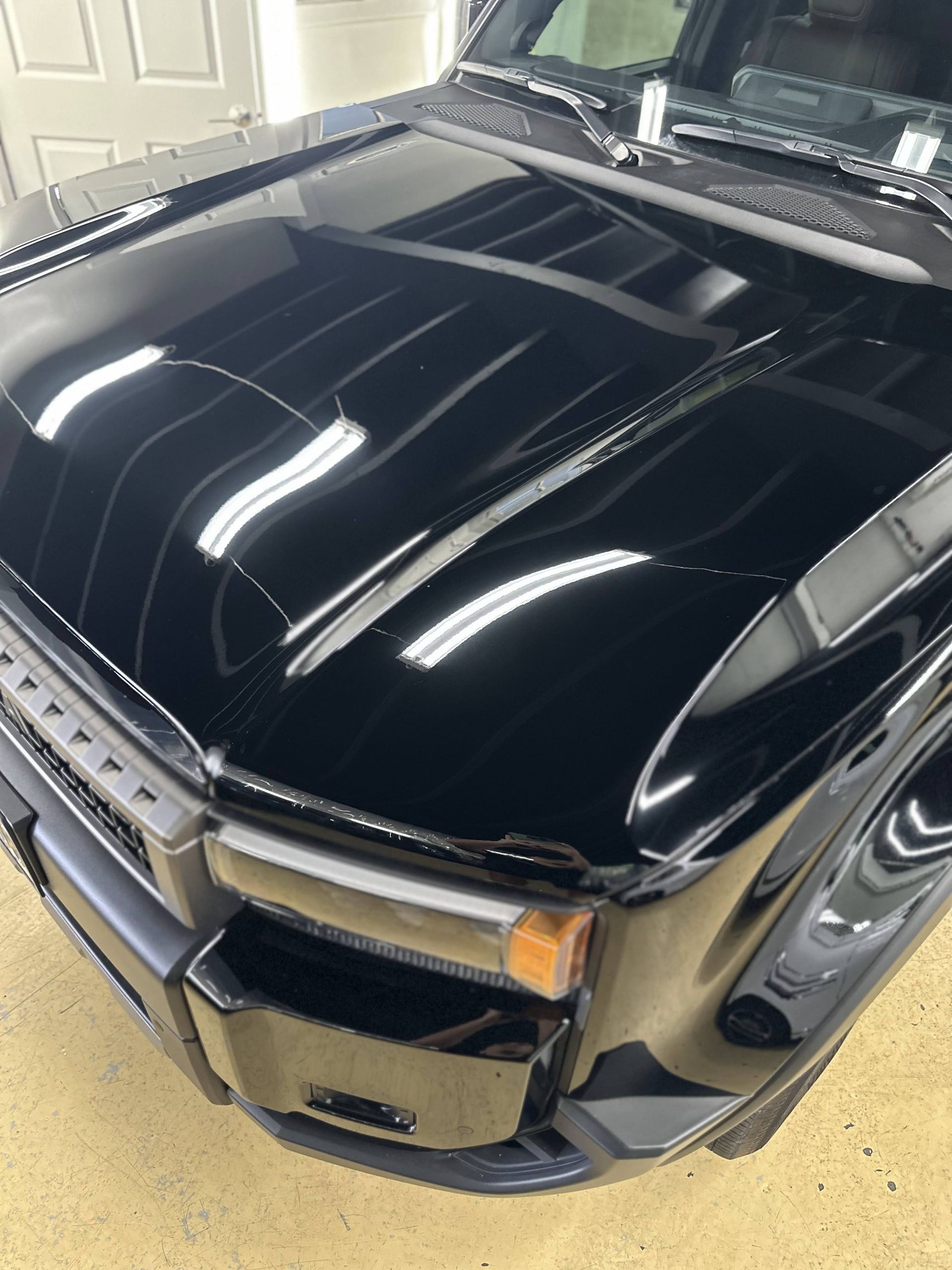Glossy black car hood and front end reflecting overhead lights in a garage