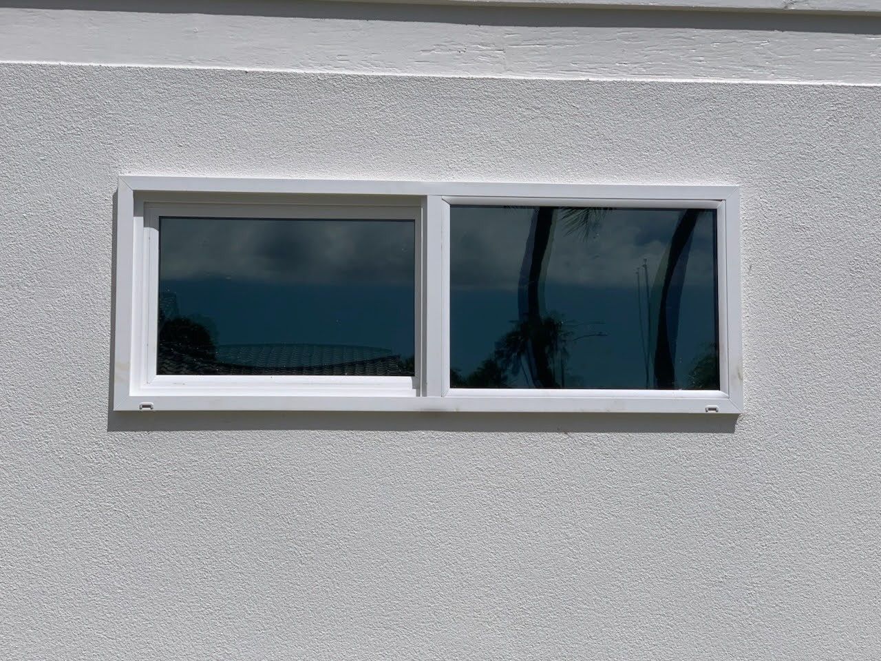 White-framed rectangular window in a gray stucco wall, with dark reflections in the glass.