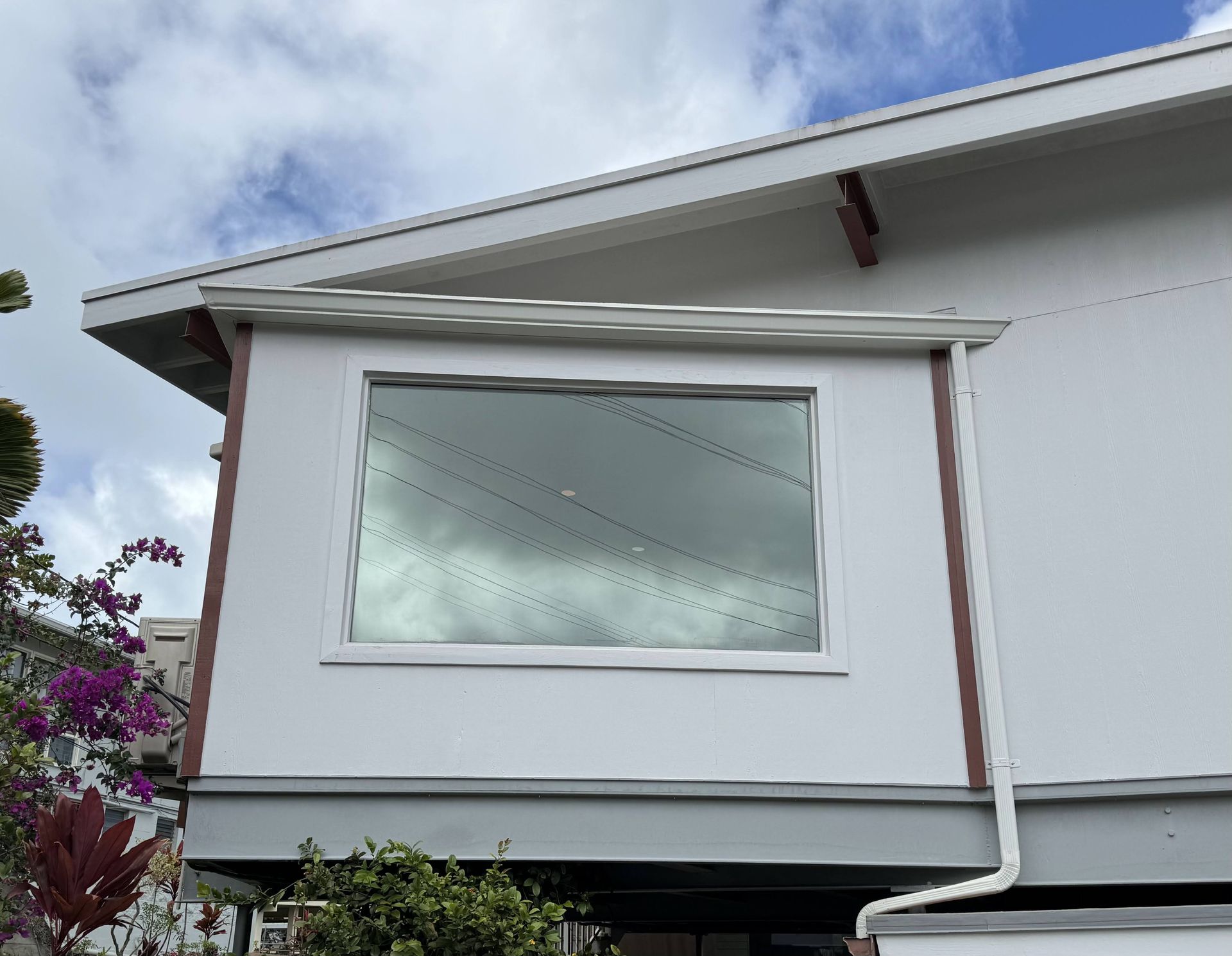 White house exterior with a large rectangular window and visible gutter under the roofline