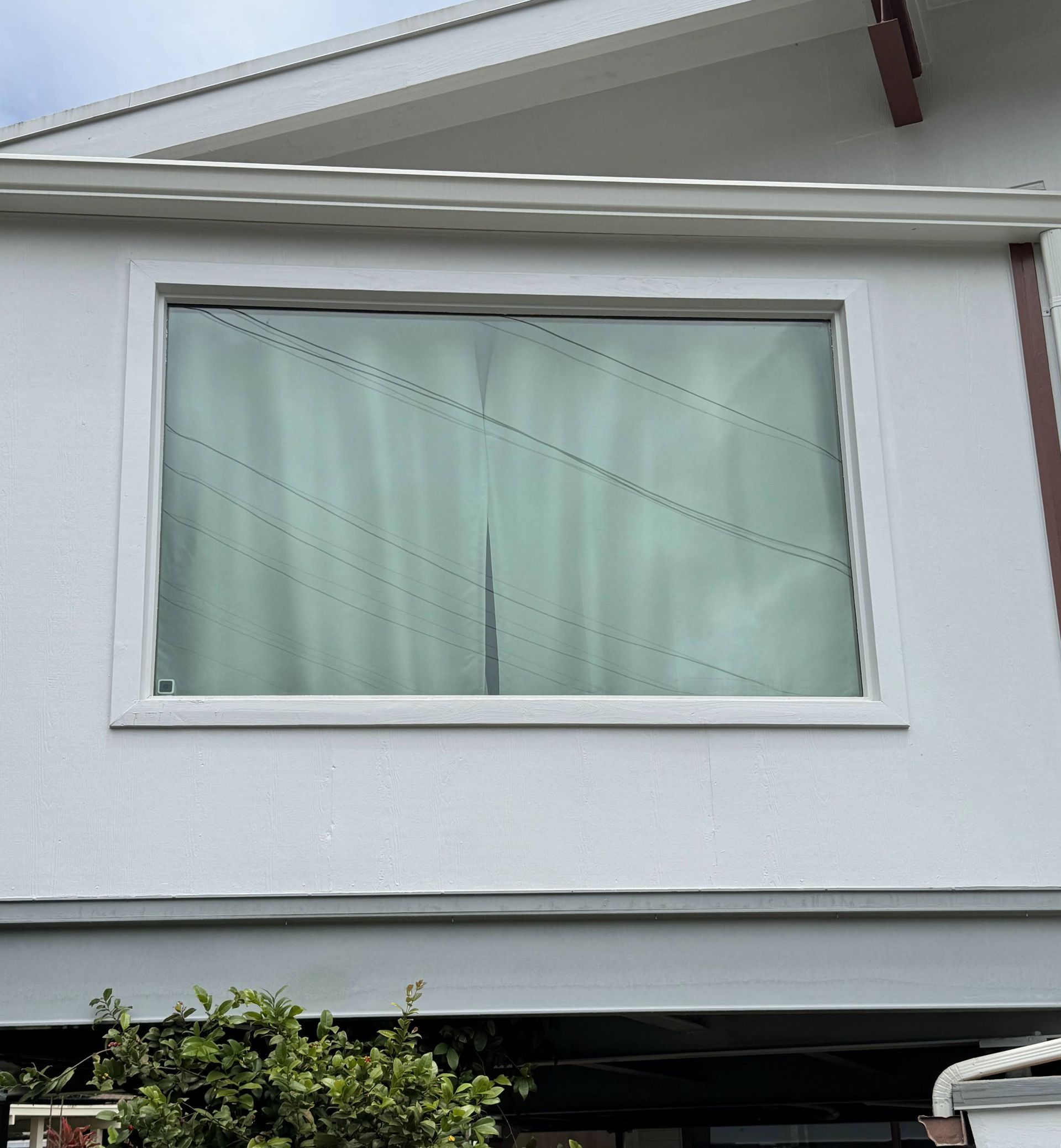 White house exterior with a large window and pale curtains beneath the roofline